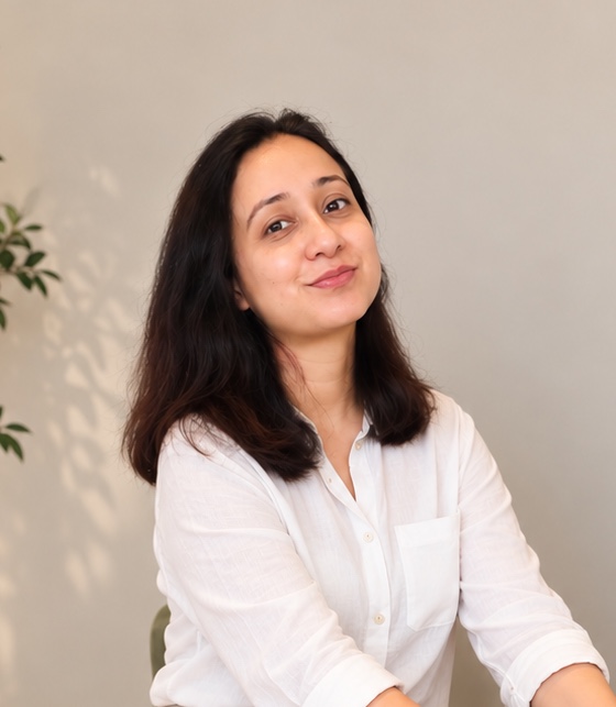 Vishali Bhagat in a white shirt, smiling towards the camera, with a plant on the wall behind her.